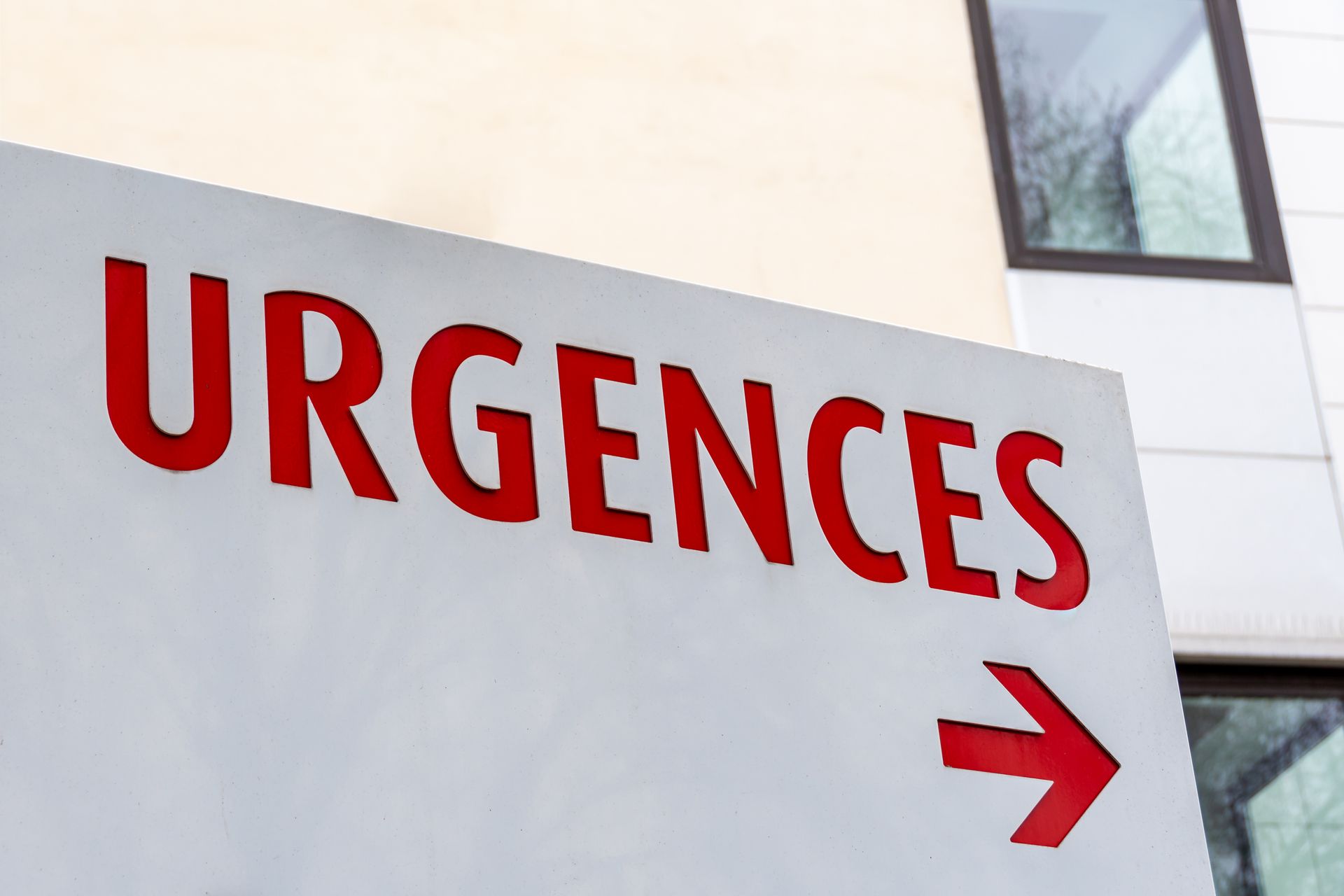 Panneau rouge URGENCES avec une flèche pointant vers la droite sur la façade d'un bâtiment.