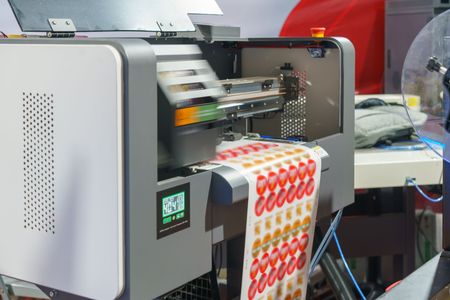 Machine d'impression d'étiquettes appliquant des autocollants sur des feuilles dans un atelier.