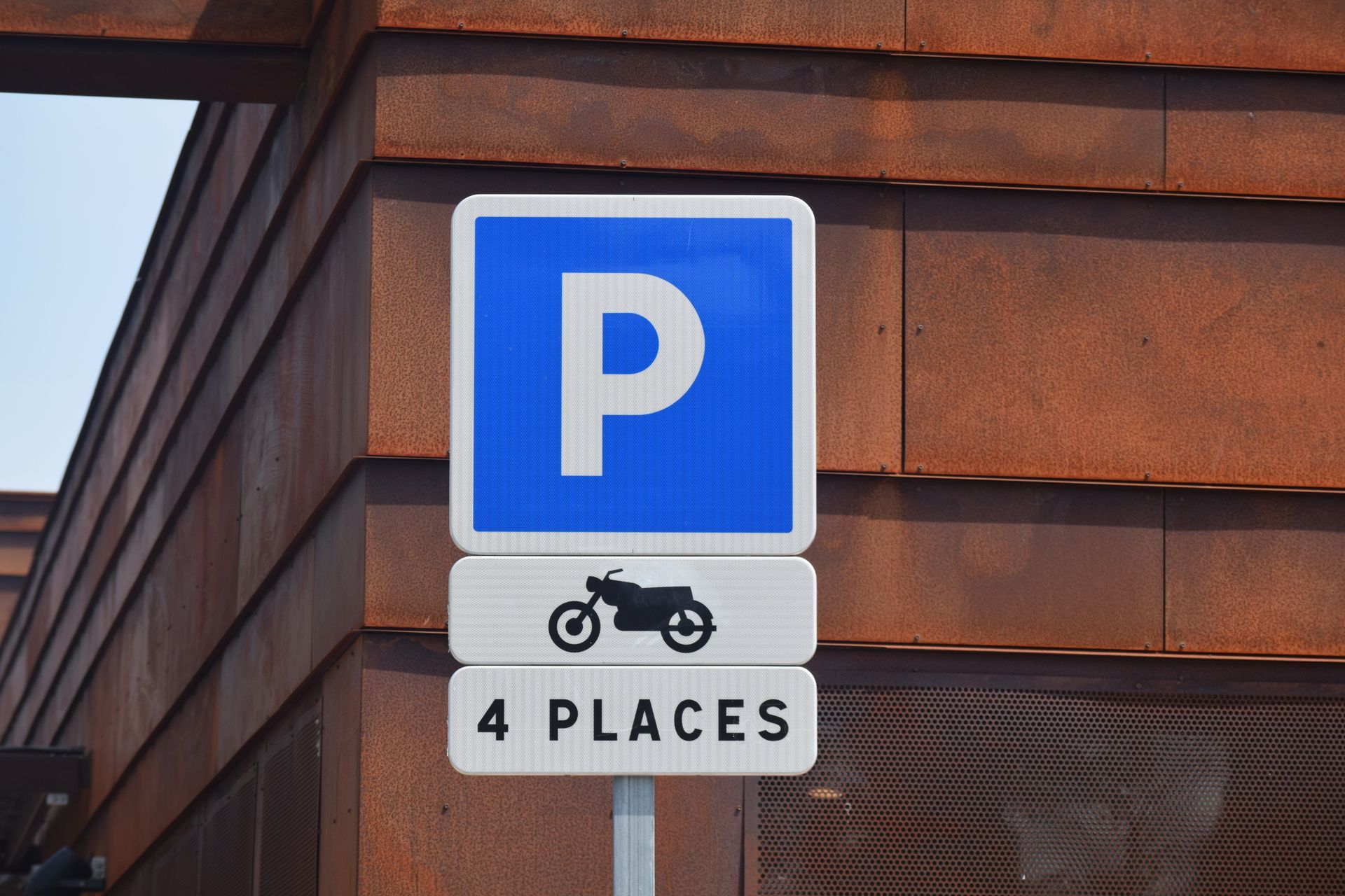 Panneau de stationnement bleu avec symbole de moto sur un mur de briques.
