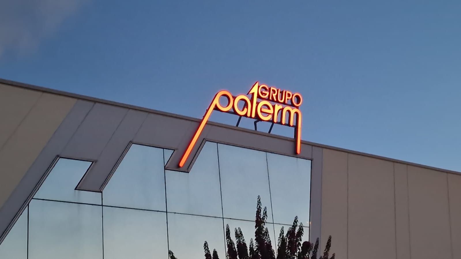 Fachada de edificio moderno con ventanas espejadas y un letrero de neón naranja "Grupo Adler" en la parte superior.