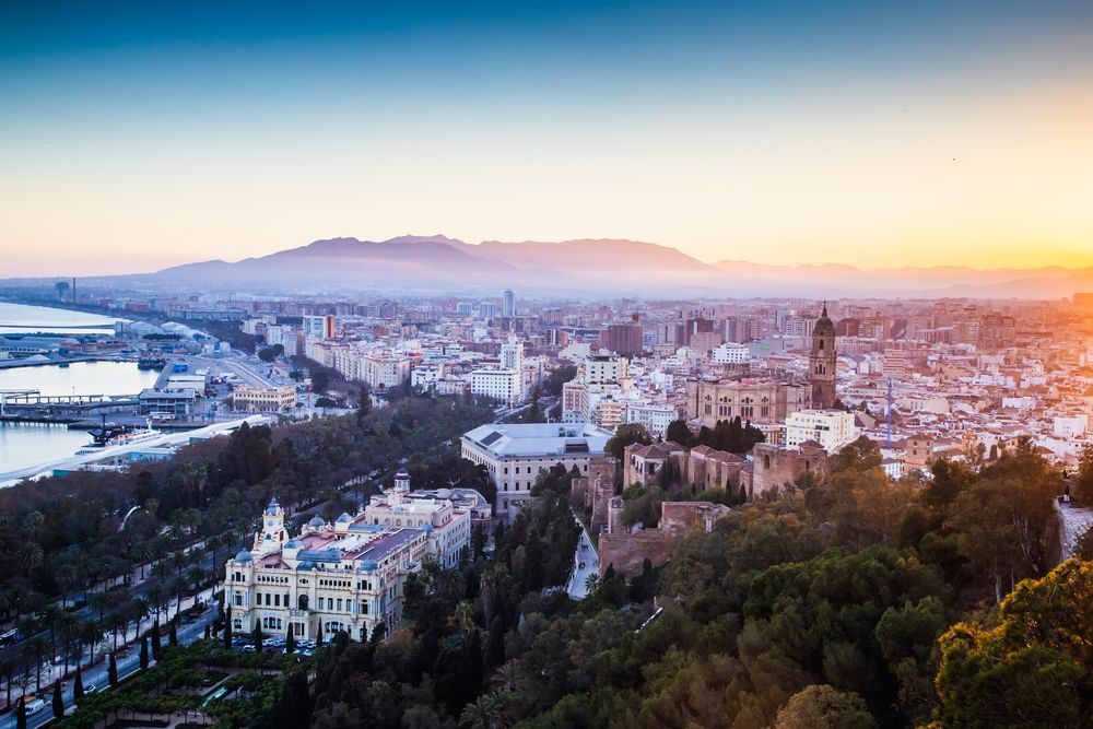 Una vista aérea de una ciudad al atardecer con montañas al fondo.