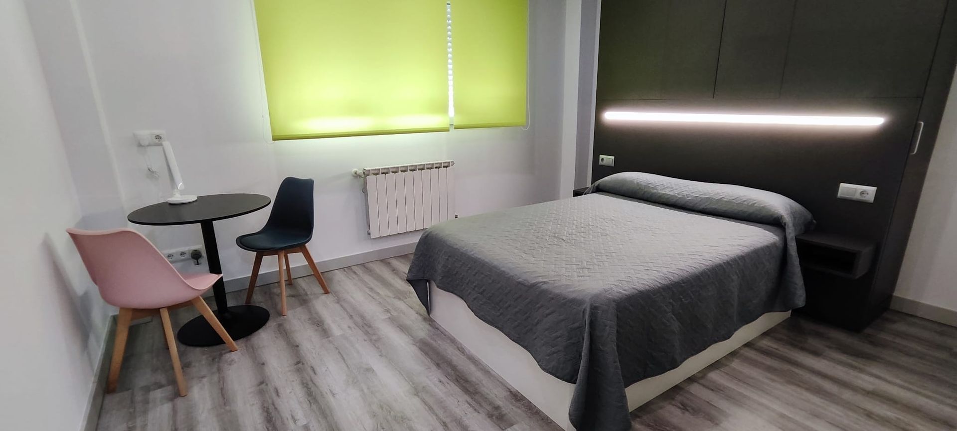 Un dormitorio moderno con una cama, dos sillas, una mesa y una persiana verde.