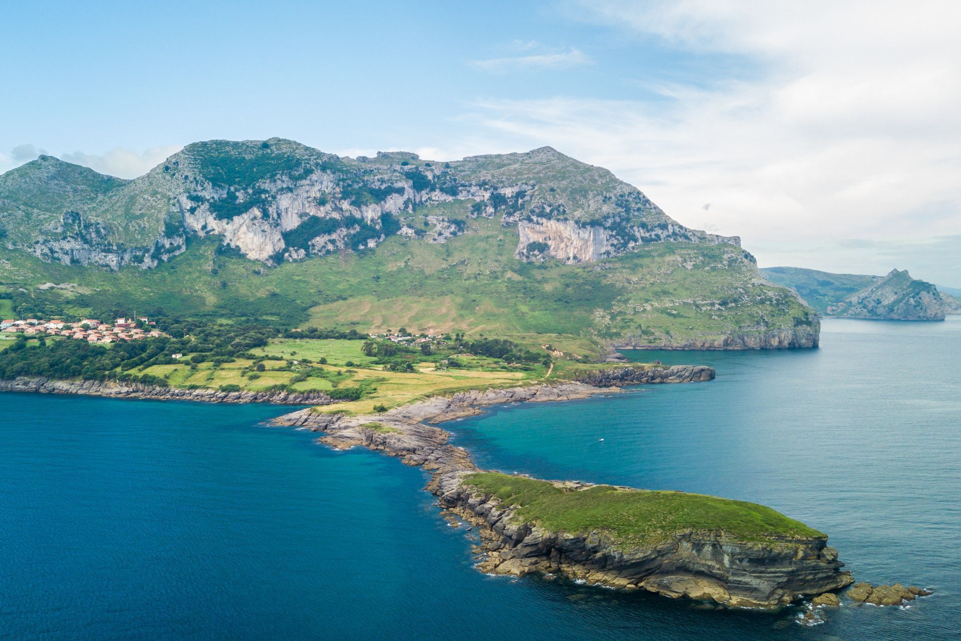 Vista costera con montañas, tierra verde, mar azul y una pequeña isla.