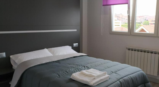 Dormitorio con ropa de cama gris, toallas blancas, ventana con persiana morada y radiador.