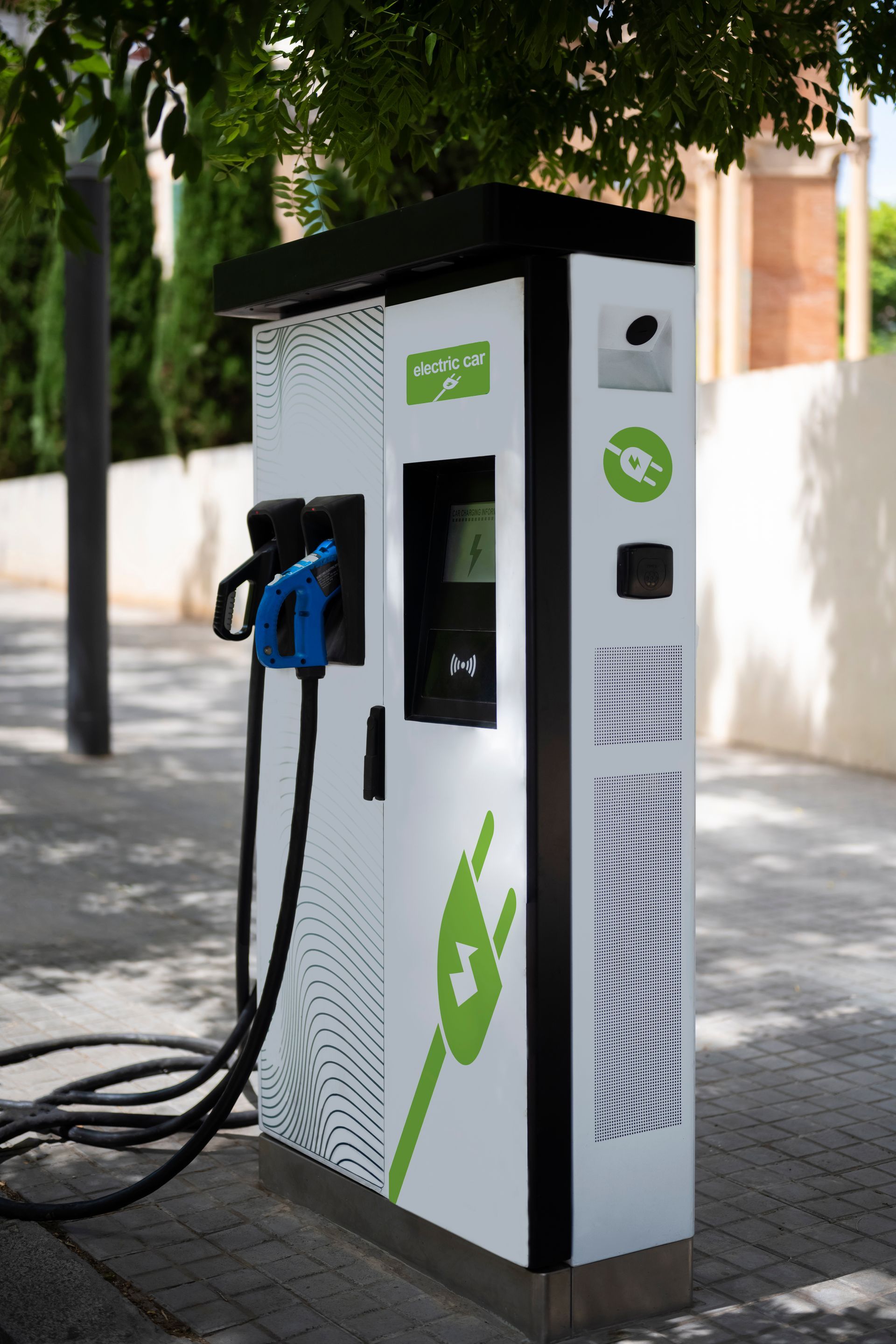 Borne de recharge pour véhicules électriques avec câble bleu sur un trottoir bordé d'arbres