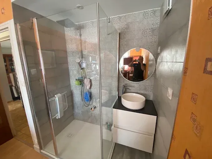 Salle de bains moderne avec douche en verre, lavabo et miroir rond sur murs carrelés gris