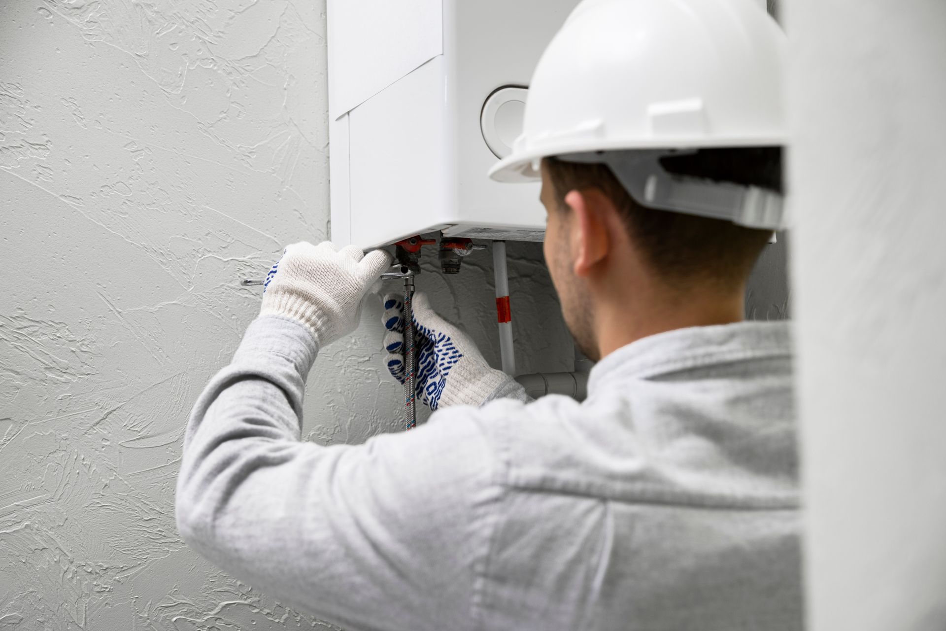Électricien portant un casque blanc, effectuant le câblage d'un tableau électrique dans un mur gris