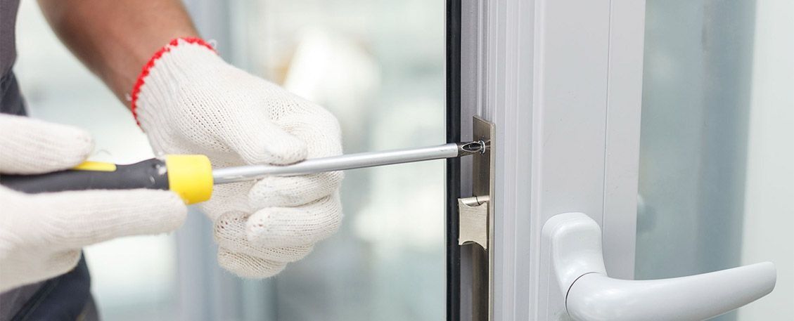 Persona con guantes que utiliza un destornillador para arreglar una puerta blanca.