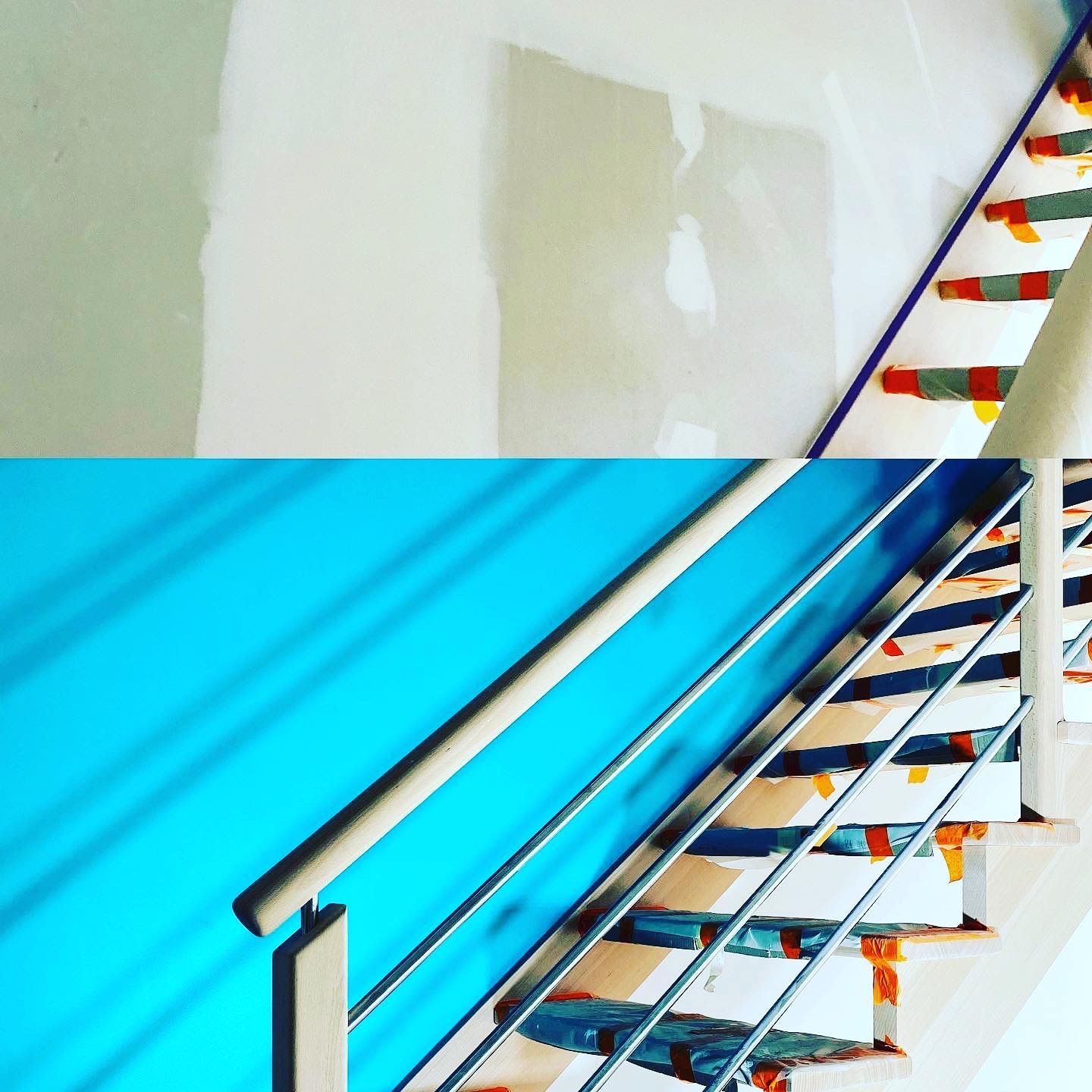 Escalier avec rampe métallique et murs bleus et vert clair. Les marches sont rehaussées de touches orange et rouge.