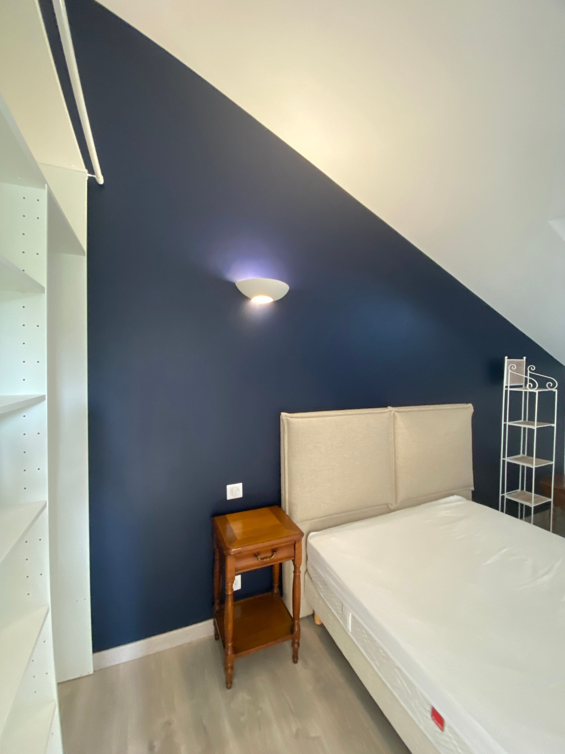 Chambre avec un mur d'accent bleu, un lit, une table de chevet et des étagères.