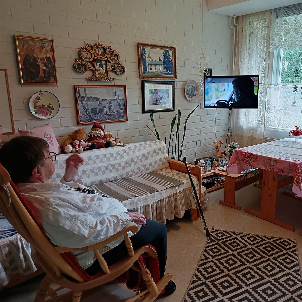 Keinutuolissa istuva vanhempi ihminen katsoo televisiota viihtyisässä huoneessa.