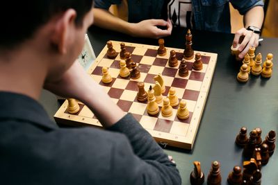Des personnes jouent aux échecs sur un échiquier en bois, les pièces capturées étant éparpillées aux alentours.