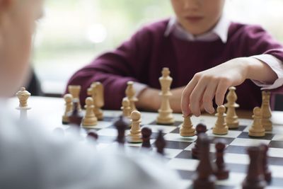 Enfant déplaçant des pièces d'échecs sur un échiquier, vêtu d'un pull bordeaux, dans un décor lumineux ressemblant à une salle de classe.