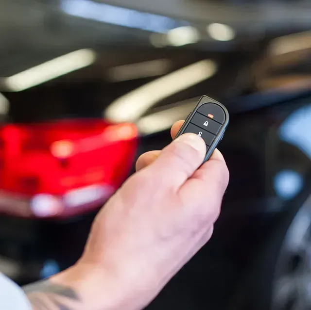 Una persona sostiene un control remoto frente a un automóvil.