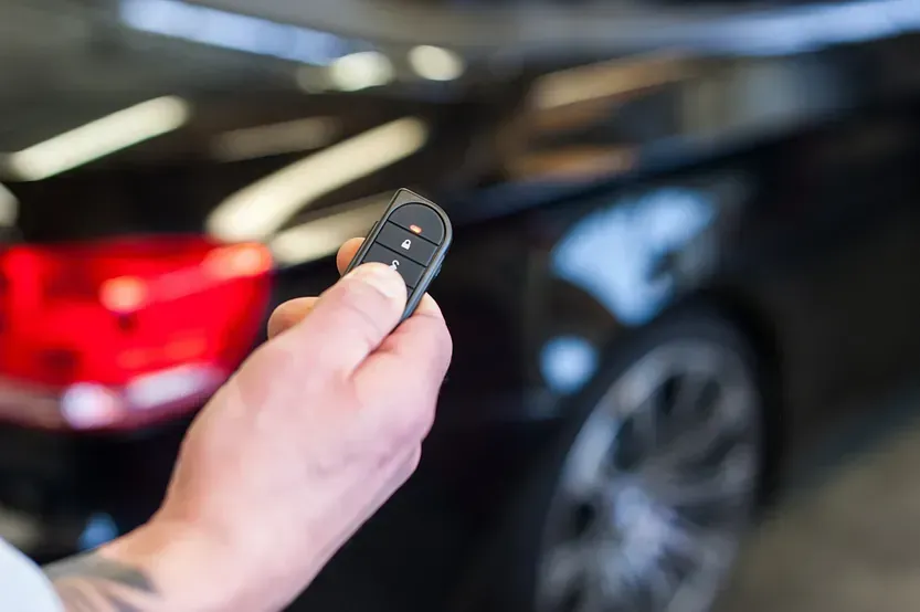 Una persona sostiene un control remoto delante de un coche.