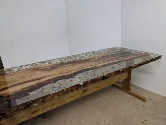 Mesa de madera con río de epoxi en el centro, contra una pared blanca.