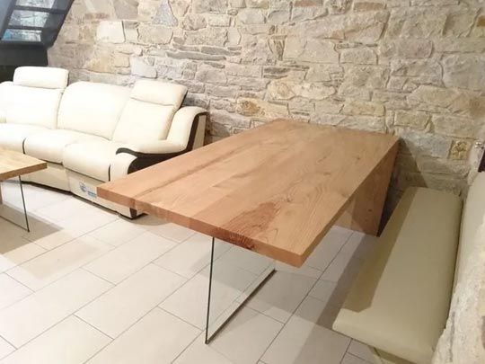 Mesa de madera adosada a una pared de piedra con un banco; sofá color crema al fondo.