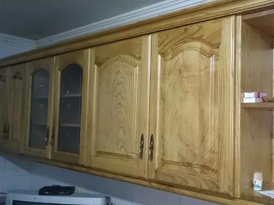 Gabinetes de cocina de madera con tallados detallados y puertas con frente de vidrio, montados en una pared.
