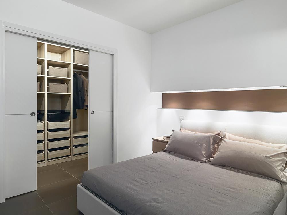 Dormitorio con puertas corredizas de armario que se abren y revelan un espacio de almacenamiento organizado. Tonos neutros, diseño moderno.