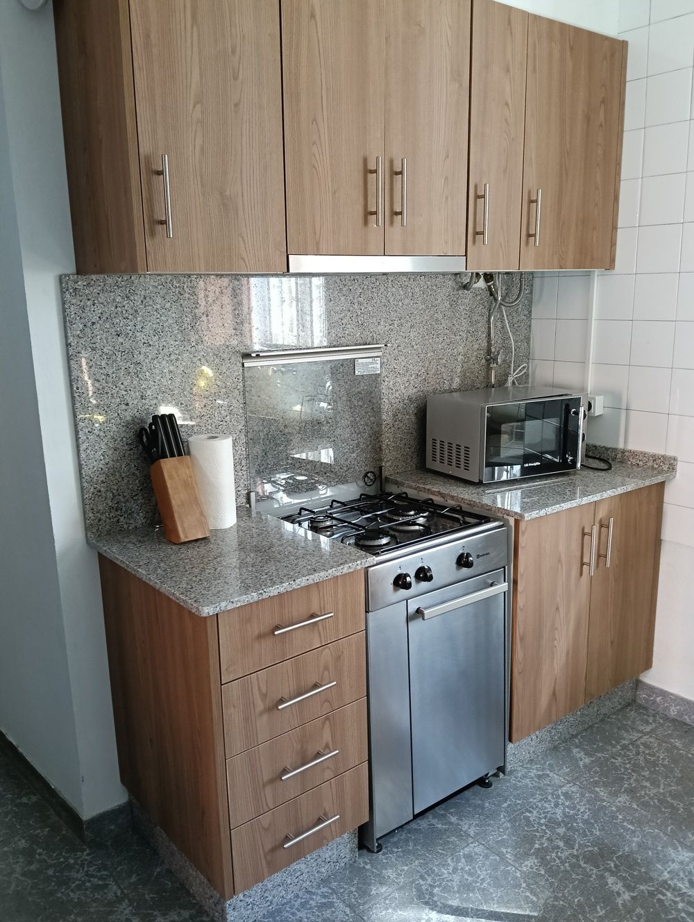 Pequeña cocina con gabinetes de madera, encimeras de granito y electrodomésticos de acero inoxidable.