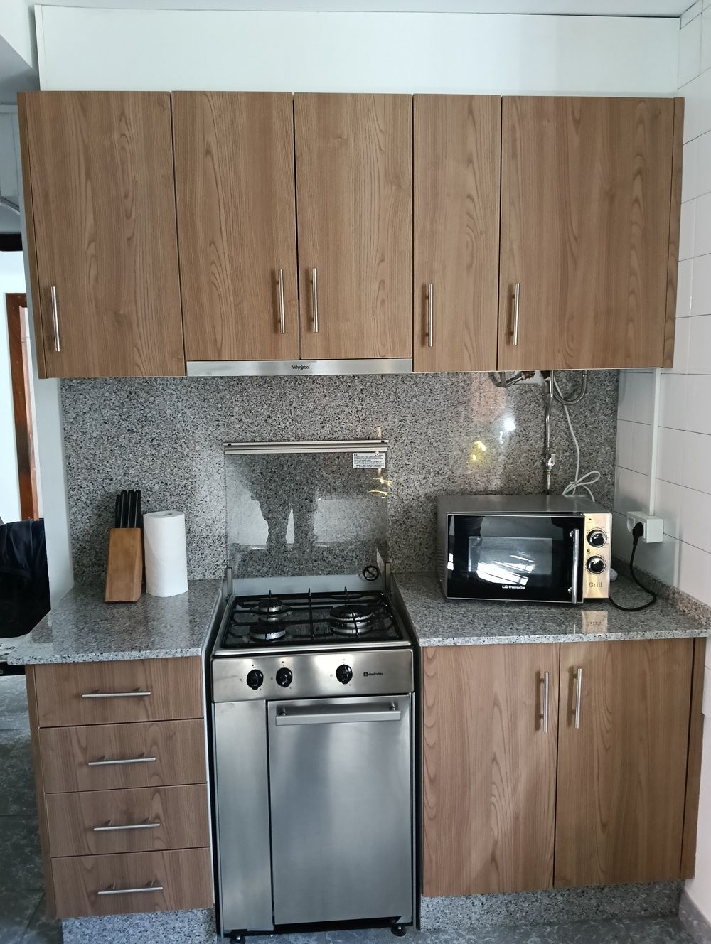 Cocina con gabinetes de madera, estufa de acero inoxidable y microondas sobre encimera.
