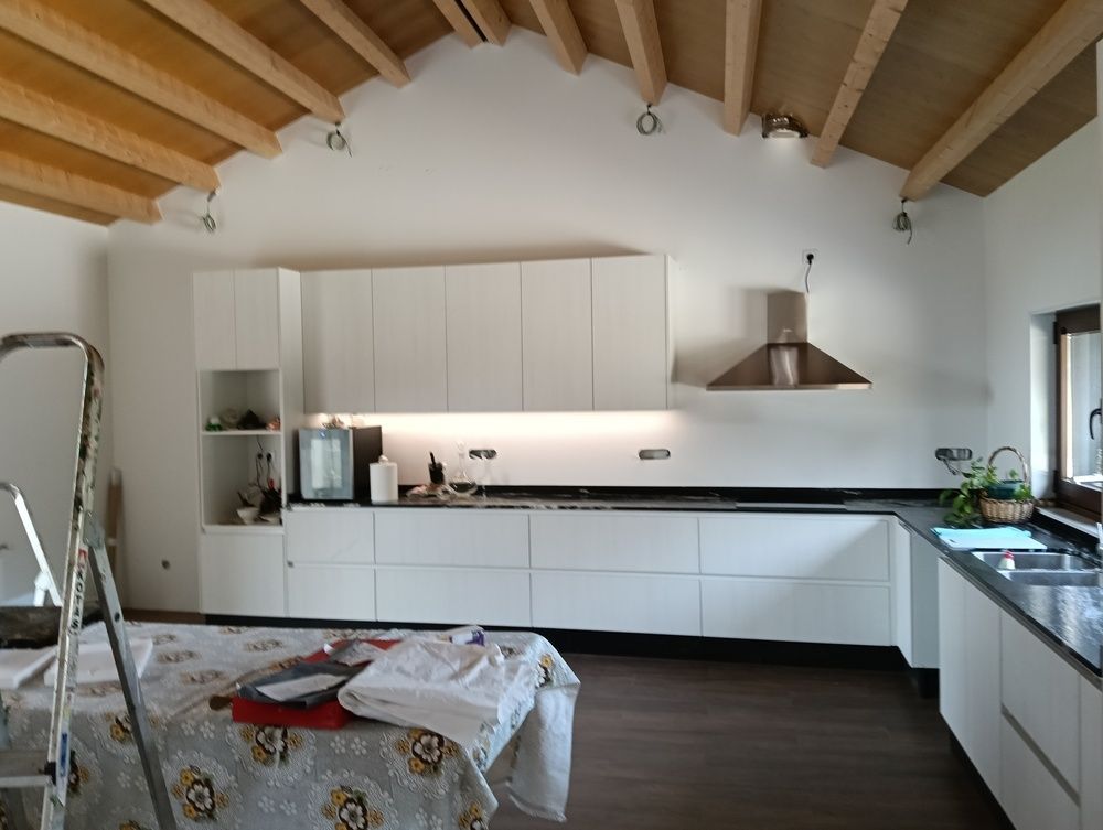 Cocina blanca moderna con techo con vigas de madera, gabinetes y campana extractora de acero inoxidable.