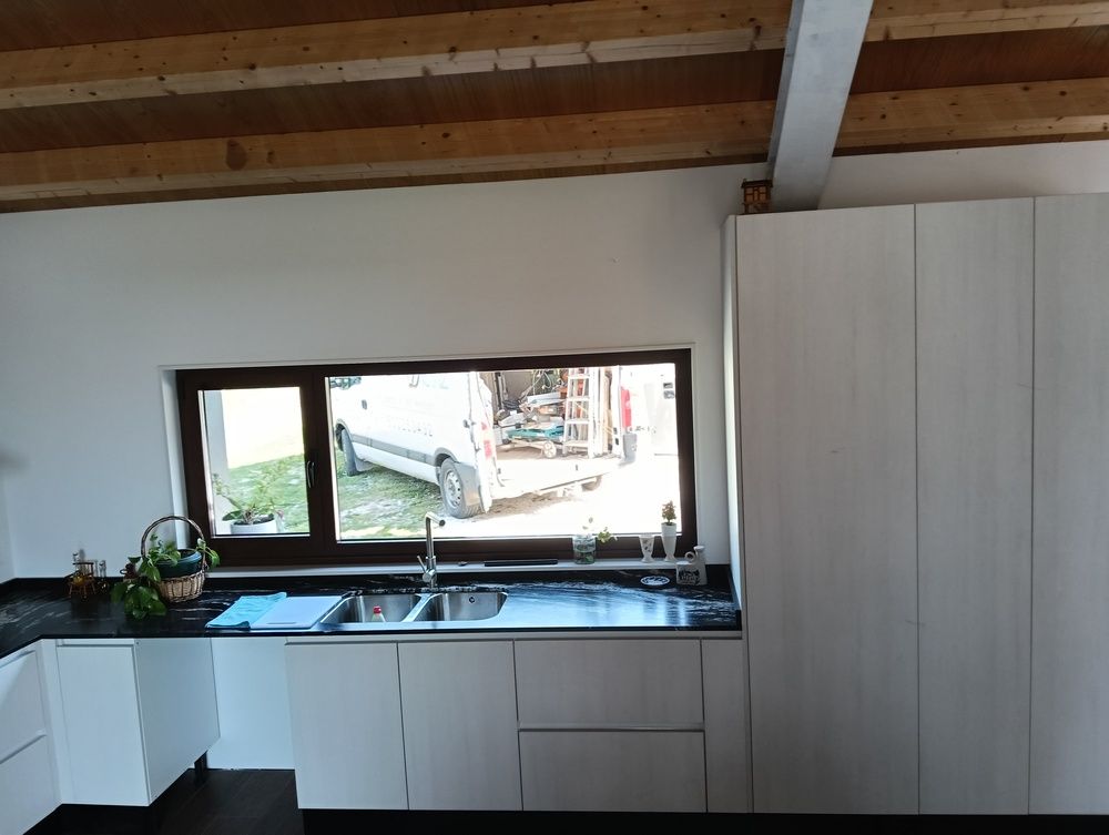 Cocina blanca moderna con encimeras negras, ventana sobre el fregadero.