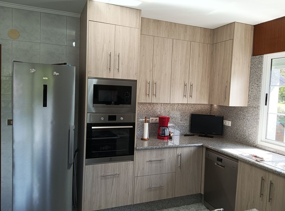 Cocina con gabinetes de madera clara, electrodomésticos de acero inoxidable y ventana.