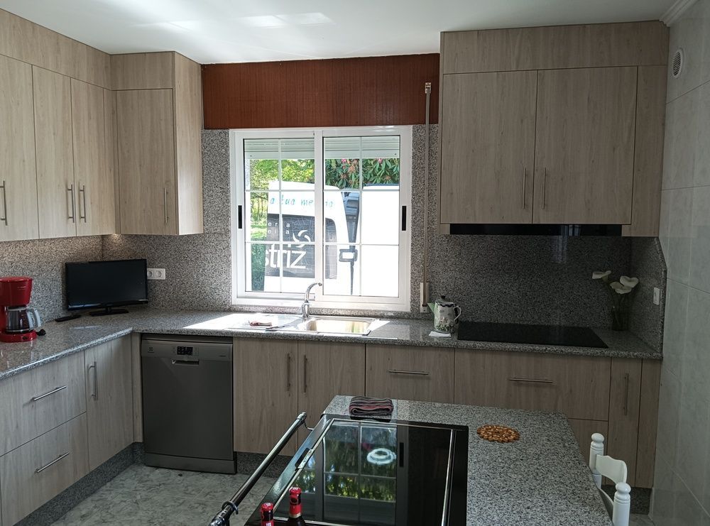 Una cocina con vetas de madera de color claro, con encimeras de granito, electrodomésticos de acero inoxidable y una isla central con anafe.