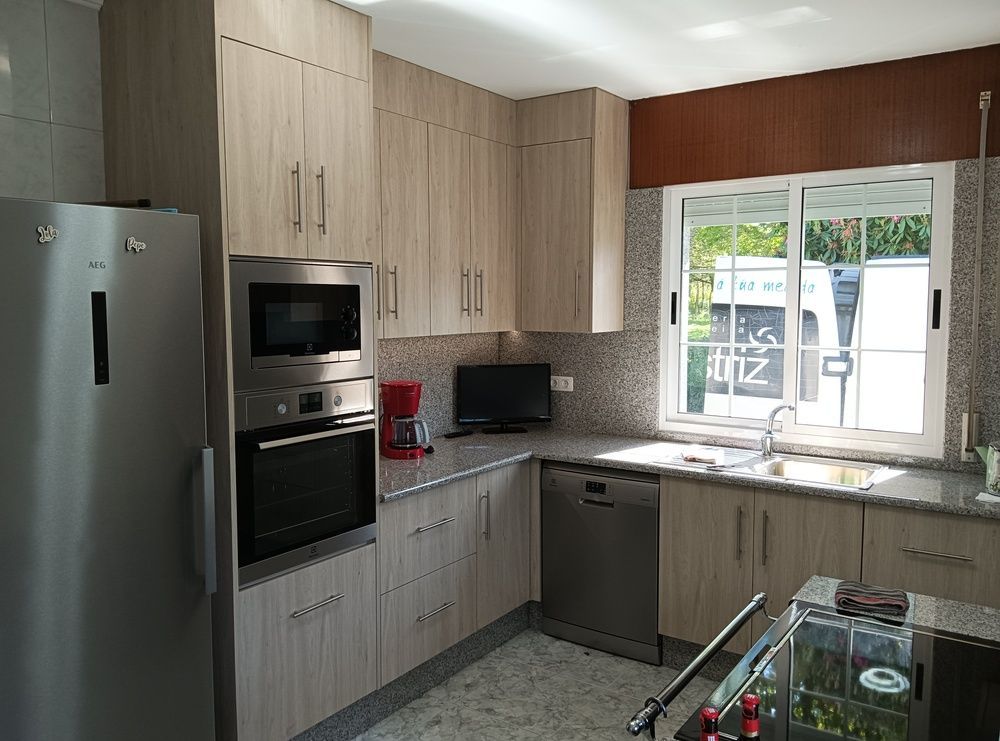 Cocina con gabinetes de madera clara, electrodomésticos de acero inoxidable y una ventana sobre el fregadero.