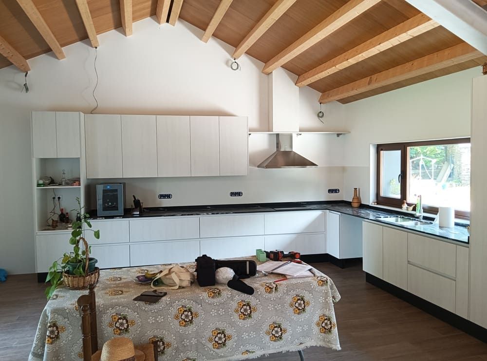 Cocina con gabinetes blancos, encimeras negras, techo de madera y una mesa grande.