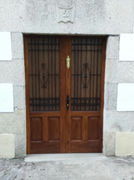 Puertas dobles de madera con rejas de hierro negro, llamador de latón y marco de piedra.