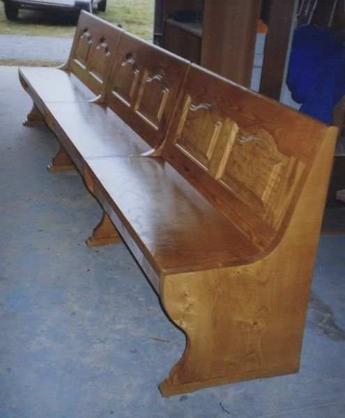 Banco de madera con respaldo para exterior. Acabado marrón claro y diseño ornamentado.