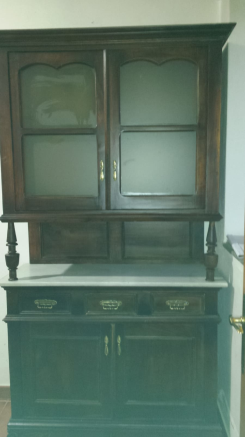 Aparador de madera oscura con armario superior con frente de vidrio, cajones y armario inferior, contra una pared.