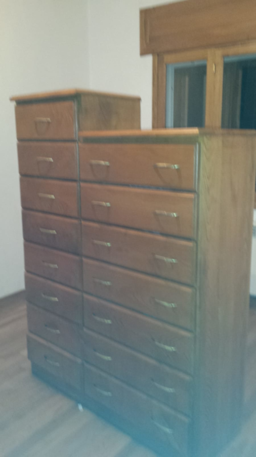 Cómoda de madera con múltiples cajones, situada contra una pared con ventana.