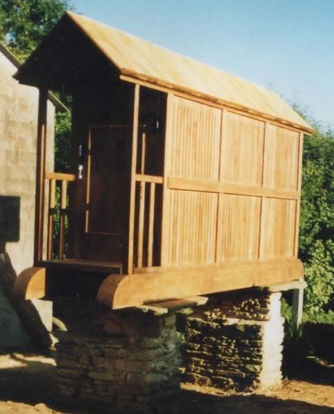 Refugio de madera sobre base de piedra, con techo cubierto y paredes de tablones verticales.