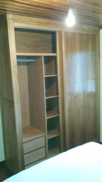 Armario de madera con puerta corrediza, estantes y cajones, en un dormitorio.