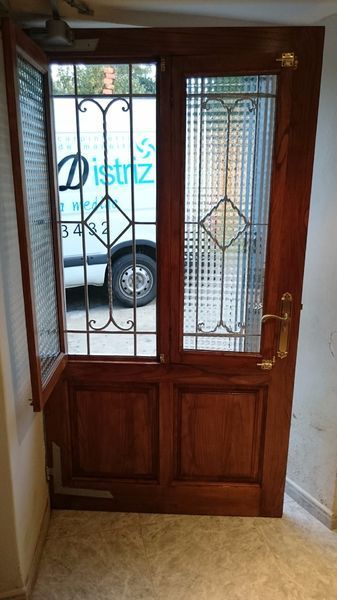 Puertas dobles de madera con paneles de vidrio y barras de metal; una camioneta blanca es visible a través de la puerta abierta.