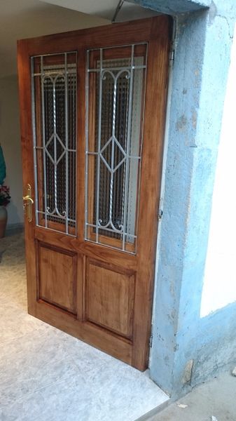 Puerta doble de madera con paneles de vidrio y herrajes decorativos, ubicada en el exterior de un edificio.