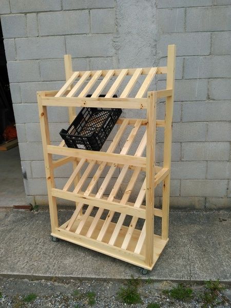 Estantería de exhibición de productos de madera con estantes en ángulo, que contiene una caja negra y está colocada contra una pared de ladrillos.