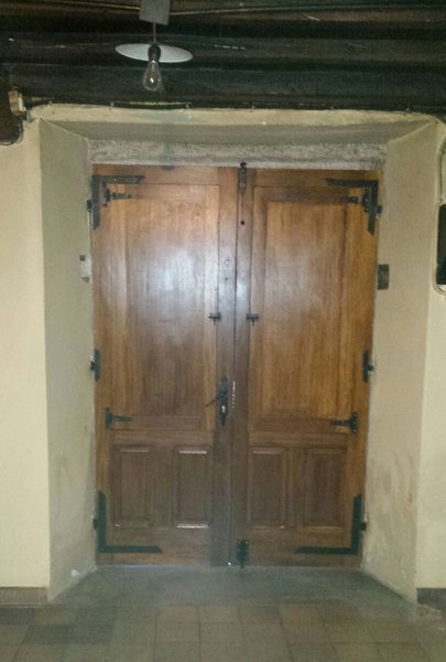 Puertas dobles de madera con herrajes negros, enmarcadas en beige. Vigas oscuras en el techo y bombilla sin bombilla.