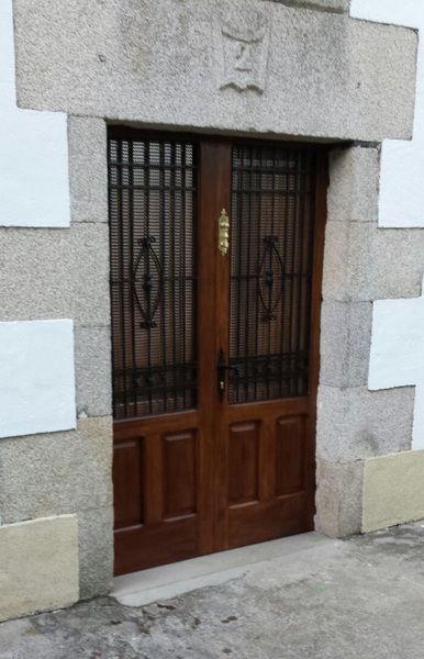 Puertas dobles de madera con rejas de seguridad de hierro negro y herrajes de latón colocados en un marco de piedra.