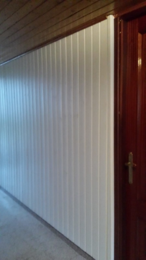 Pared de paneles blancos verticales con puerta y molduras de madera oscura.