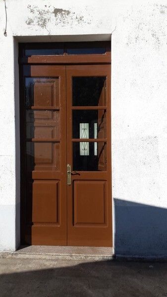 Puertas dobles marrones en una pared blanca con paneles de vidrio y una pequeña ventana encima.