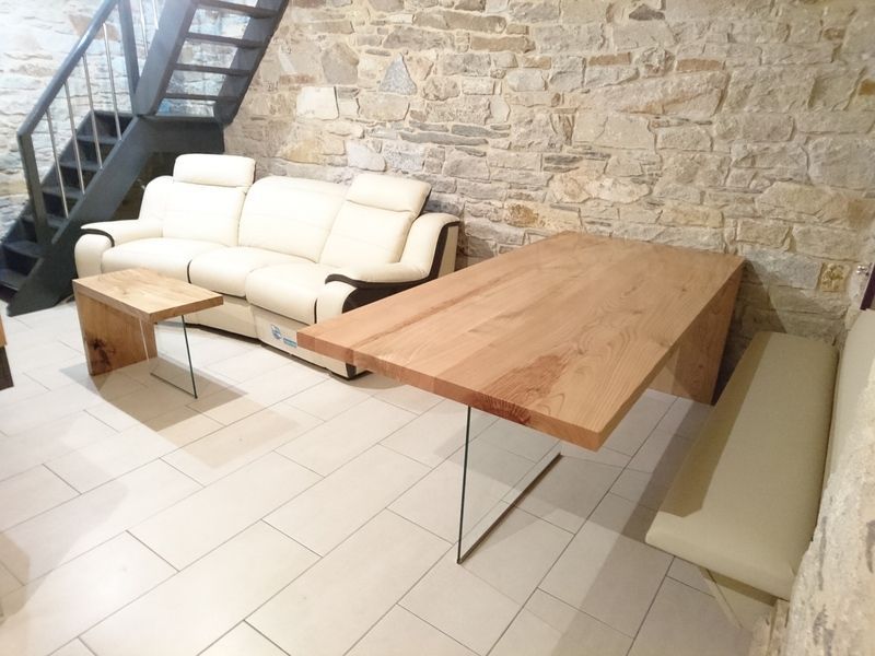Sala de estar con sofá de cuero blanco, mesa de madera, banco y pared de piedra.