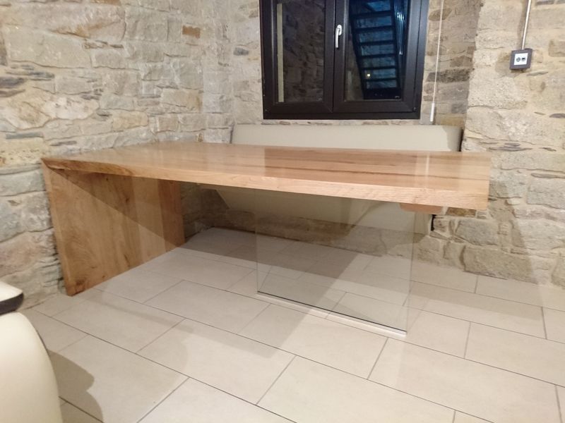 Escritorio de madera adosado a una pared de piedra, bajo una ventana. Suelo de baldosas color crema.