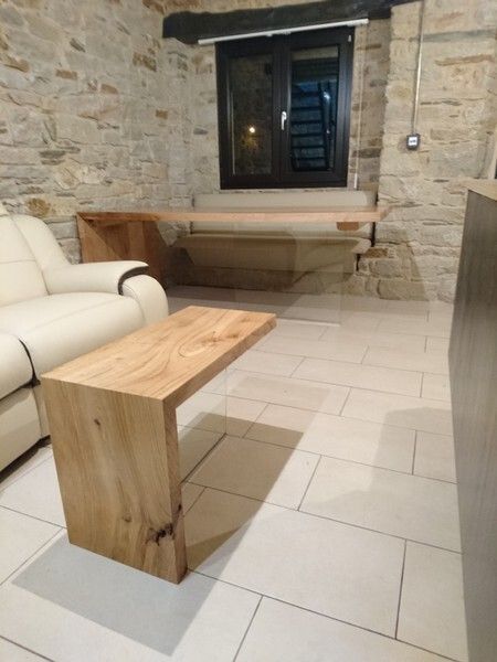Mesa de centro de madera y banco empotrado en una habitación con paredes de piedra y ventana.