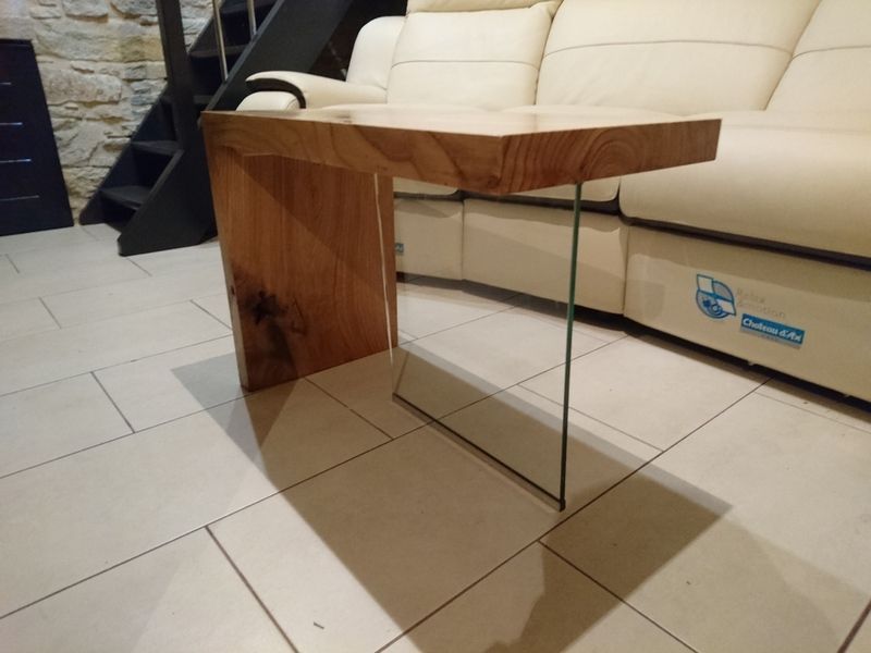 Mesa auxiliar de madera con pata de cristal junto a un sofá color crema.