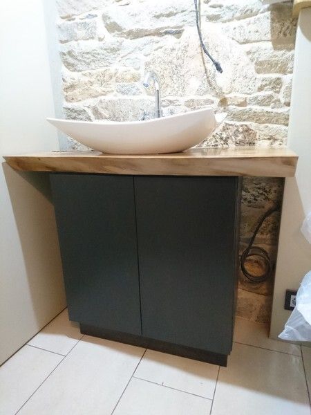 Tocador de baño con lavabo de encimera, mueble gris oscuro y fondo de pared de piedra.