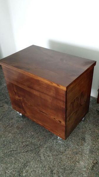 Baúl de almacenamiento de madera con acabado marrón oscuro, colocado sobre una superficie moteada de color gris.